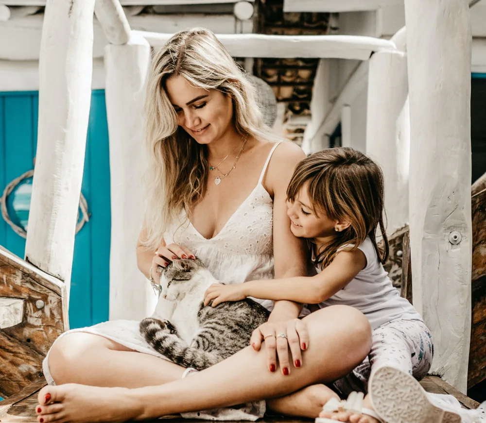 Femme et enfant caressant un chat gris tigré après le brossage — routine douce pour limiter la mue d’automne.